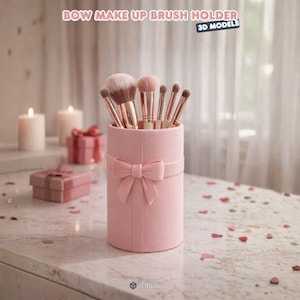 Puede incluir: Un portalápices de maquillaje cilíndrico rosa con un detalle de lazo, lleno de varios pinceles de maquillaje. El soporte está sobre una superficie de mármol, con velas y cajas de regalo en el fondo. El texto en la parte superior dice "BOW MAKE UP BRUSH HOLDER".