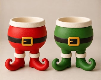 Op de afbeelding: Twee kommen in de vorm van benen met gekrulde tenen, één rood en één groen, elk met een zwarte riem met een gele gesp en een witte, getextureerde rand. De tekst CHRISTMAS GRINCH LEGS BOWL en 3D STL-MF MODELS staat bovenaan de afbeelding.