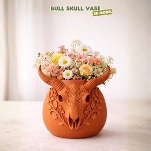 Puede incluir: Un jarr&oacute;n de calavera de toro de color terracota, adornado con un dise&ntilde;o detallado de calavera de toro y motivos florales, contiene un vibrante ramo. Las flores incluyen margaritas, rosas y otras flores en tonos de rosa, amarillo y blanco. El texto de la imagen dice "BULL SKULL VASE" y "3D MODEL".