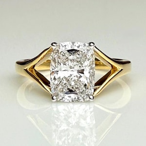 Könnte beinhalten: Ein Goldring mit einem großen, rechteckigen Diamanten im Kissenschliff, der in einer Vier-Krappen-Fassung sitzt. Die Ringschiene hat ein geteiltes Design, das zum Mittelstein hin schmaler wird und eine polierte, reflektierende Oberfläche bietet.