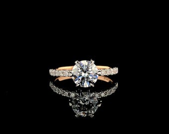 May include: A diamond engagement ring with a round brilliant center stone and a pave diamond band. The ring is set in rose gold.