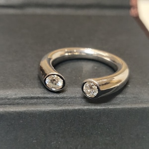 May include: A silver ring with two round diamonds set into the band. The ring is open on one side.