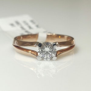 Könnte beinhalten: Ein Verlobungsring aus Roségold mit einem einzelnen runden Diamanten, der in einer Weißgoldfassung sitzt. Der Ring hat ein geteiltes Banddesign.