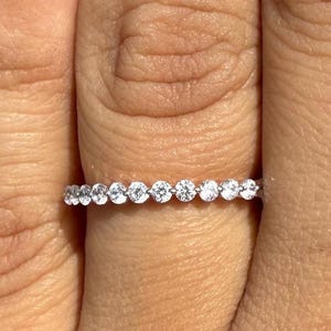 Può includere: Primo piano di un anello d'argento con una serie di piccole pietre preziose rotonde e trasparenti. L'anello è su un dito e le pietre preziose brillano alla luce. Un gioiello delicato.
