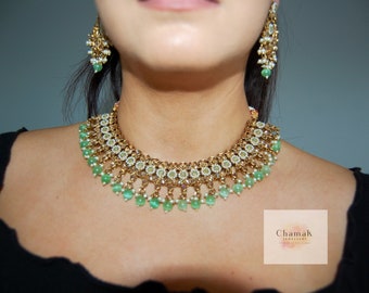 May include: A gold and green necklace and earrings set with white stones. The necklace has a layered design with green beads and the earrings are long and dangle.