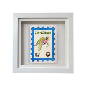 Peut inclure: Une œuvre encadrée représentant un timbre-poste avec le mot "ZANZIBAR" en vert et une illustration de tortue marine. Le timbre a une bordure bleue et une petite icône de singe.