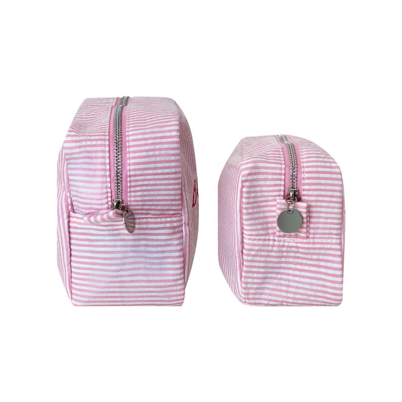 Puede incluir: Dos neceseres a rayas rosas y blancas. Las bolsas tienen cremalleras plateadas y un peque&ntilde;o dije plateado en el tirador de la cremallera. La bolsa m&aacute;s grande tiene la letra "B" bordada en rojo. Las bolsas son rectangulares y tienen la parte superior redondeada.
