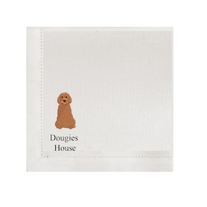 Op de afbeelding: Witte vierkante linnen servet met een geborduurd beeld van een golden doodle hond. De tekst "Dougies House" is eronder geborduurd. De servet heeft een gestikte rand.