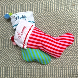 May include: Two Christmas stockings with white fabric and red and pink stripes, and green and blue stripes. The stockings are embroidered with the words "Daddy" and "Mummy".