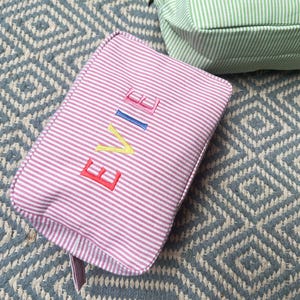 May include: Pink striped makeup bag with the name "EVIE" embroidered in colorful letters.