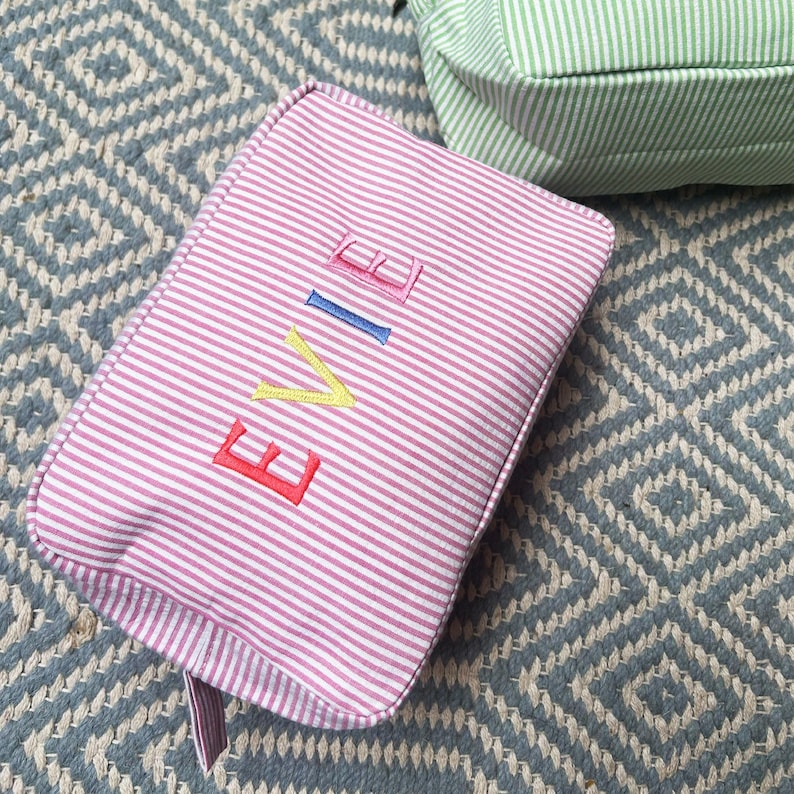 May include: Pink striped makeup bag with the name "EVIE" embroidered in colorful letters.