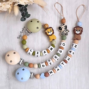 Può includere: Tre morsi per bambini in silicone con clip. Un morso è verde con tre fori e ha il nome "Liam" scritto in perle bianche. Un altro morso è beige con tre fori e ha il nome "D.I.D" scritto in perle bianche. Il terzo morso è blu con tre fori e ha il nome "Nathan" scritto in perle bianche. Ogni morso ha un ciondolo animale diverso: un leone, una zebra e un orso.