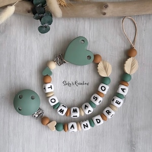 Può includere: Un mordedor per neonati in silicone verde e marrone con il nome "Thomas Andre" scritto in perle bianche. Il mordedor ha un clip per fissarlo ai vestiti e un piccolo pezzo di silicone a forma di cuore.