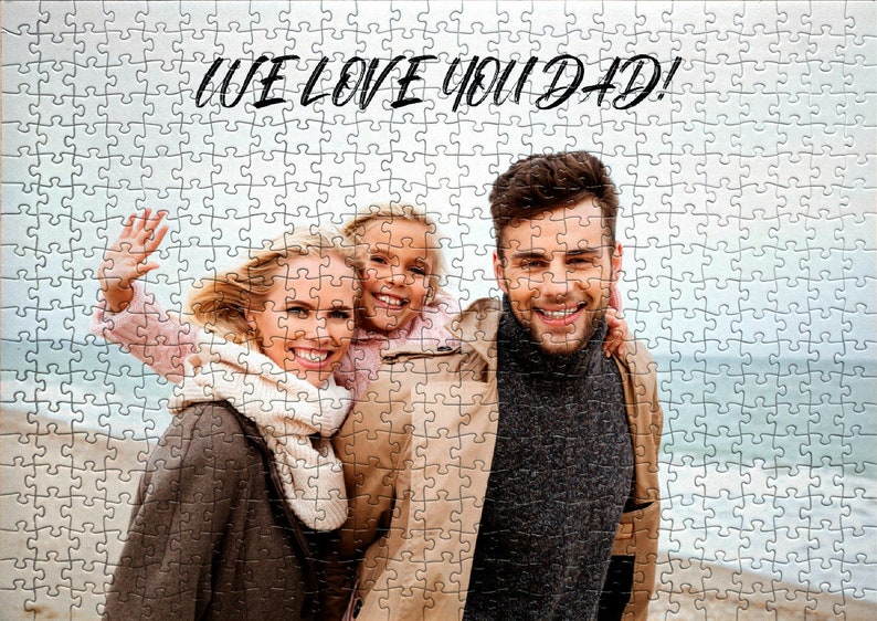 May include: A family of three, a woman, a girl, and a man, are smiling at the camera. The woman is wearing a brown coat and a white scarf. The girl is wearing a pink shirt. The man is wearing a brown coat and a gray sweater. The text "WE LOVE YOU DAD!" is written in black at the top of the image.