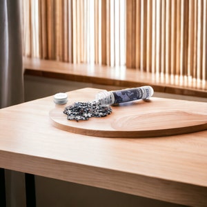 May include: A wooden table with a round wooden tray on top. A clear plastic tube with a map design and the word "ECONOMIA" printed on it is lying on the tray. A small pile of black and white puzzle pieces is scattered on the tray.