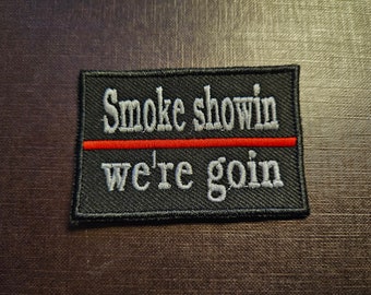 May include: Black embroidered patch with white text that reads "Smoke showin' we're goin'" with a red line separating the two lines of text.