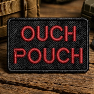 May include: A rectangular black patch with a stitched border featuring the text OUCH POUCH embroidered in bold red capital letters. The patch has a textured fabric surface and is designed for attachment to gear or clothing items.