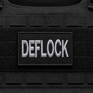 May include: A black tactical vest featuring a rectangular patch with the word DEFLOCK embroidered in silver-grey thread. The vest has a horizontal MOLLE webbing system with multiple slots for gear attachment, constructed from durable black fabric.