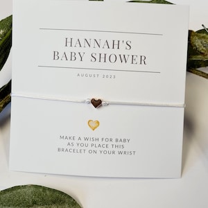 May include: A white card with the text "HANNAH'S BABY SHOWER AUGUST 2023" and a gold heart charm bracelet. The card also includes the text "MAKE A WISH FOR BABY AS YOU PLACE THIS BRACELET ON YOUR WRIST."