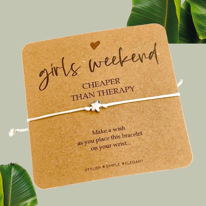 May include: A white string bracelet with a silver star charm and a card that reads "girls weekend CHEAPER THAN THERAPY" and "Make a wish as you place this bracelet on your wrist... STYLISH SIMPLE ELEGANT"