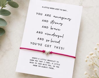 May include: A bright pink string bracelet featuring a small silver-toned heart charm, attached to a white card printed with the text: A LITTLE WISH JUST TO SAY... YOU ARE amazing AND strong AND brave AND wonderful AND so loved YOU'VE GOT THIS!