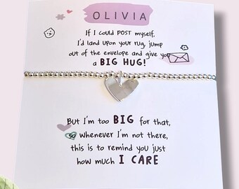May include: A silver bracelet with a heart charm is displayed on a white card. The card has text that reads "OLIVIA" and a message about sending a hug. The bracelet is a thoughtful gift.