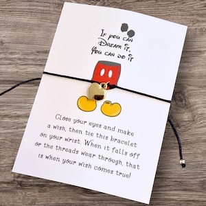 May include: A wish bracelet with a gold heart charm, black cord, and a card featuring Mickey Mouse imagery and the text "If you can dream it, you can do it." The card also includes instructions on how to use the bracelet.