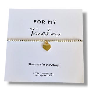 Könnte beinhalten: Ein Perlenarmband mit einem goldenen Herzanhänger auf einer weißen Karte. Die Karte enthält den Text FOR MY Teacher, Thank you for everything!, LITTLE KEEPSAKES und CHEZANDMAZ.COM. Das Armband besteht aus kleinen metallischen Perlen.