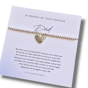 May include: A silver beaded bracelet with a heart charm, displayed on a white card. The card reads "IN MEMORY OF YOUR AMAZING Dad" and includes a heartfelt message. The bracelet is a delicate piece of memorial jewelry.