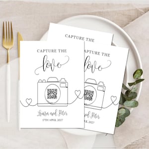 May include: White cards with the text "CAPTURE THE love" and a camera illustration. The cards include the names "Louisa and Peter" and the date "17th April 2027". The cards are on a white plate with gold and white cutlery.