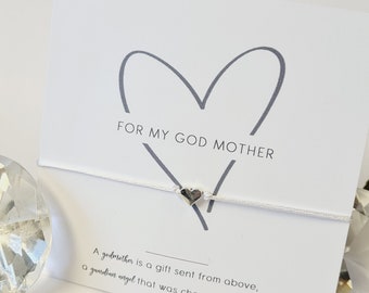 Può includere: Carta bianca con un cuore disegnato a mano e il testo "FOR MY GOD MOTHER". Sotto il cuore c'è un ciondolo d'argento a forma di cuore. Il testo sotto il ciondolo dice "A godmother is a gift sent from above, a guardian angel that was chosen with love."