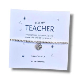 Könnte beinhalten: Ein silbernes Perlenarmband mit einem herzförmigen Kristallanhänger, präsentiert auf einer weißen Karte mit dem Aufdruck FOR MY TEACHER, YOU HELPED ME SPARKLE IN ALL I DO, THANK YOU, TEACHER, FOR BEING YOU, Love Sonai x und LITTLE KEEPSAKES.