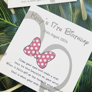 May include: A white card with a gray Mickey Mouse head design and red polka dot bow. The card says "Kelly's 17th Birthday" and "24th August 2024". The card also includes the text "Close your eyes and make a wish then tie this bracelet on your wrist. When it falls off or the threads wear through, that is when your wish comes true!"