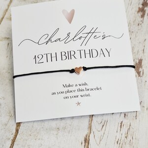 以下が含まれることがあります： 「Charlotte's 12th Birthday」と書かれた白いカードと、ローズゴールドのハートチャームが付いた黒い紐のブレスレット。カードには「このブレスレットを腕につける際に願い事をしましょう」というメッセージも書かれています。