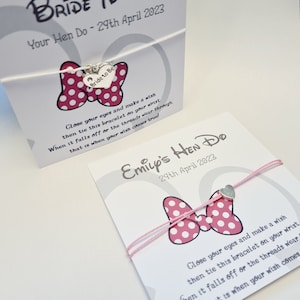May include: Two white cards with pink and white polka dot bows and silver heart charms. The cards have text that reads "Bride to Be Your Hen Do - 29th April 2023" and "Emily's Hen Do 29th April 2023". The text on the cards instructs the recipient to make a wish and tie the bracelet on their wrist. When the bracelet falls off or the threads wear through, their wish will come true.
