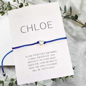 May include: A white card with the name "CHLOE" printed in black at the top. A blue string bracelet with a silver heart charm is attached to the card. The card includes instructions for making a wish and tying the bracelet on your wrist. When the cord frays, your wish will come true.