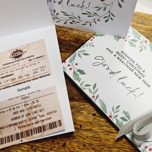 May include: A lottery ticket and Christmas greeting cards. The cards have a green and red floral border and the text "Wishing you a Merry Christmas and a Wealthier New Year." One card is tied with a grey ribbon.