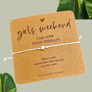 May include: A white string bracelet with a silver star charm. The card reads "girls weekend CHEAPER THAN THERAPY" and "Make a wish as you place this bracelet on your wrist... STYLISH SIMPLE ELEGANT".