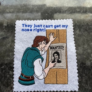 Peut inclure: Patch brodé représentant un homme de dessin animé regardant un avis de recherche avec son propre visage dessus. Le texte sur le patch est "They just can't get my nose right!"