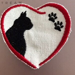 Könnte beinhalten: Roter herzförmiger Patch mit einer schwarzen Katzensilhouette und zwei Pfotenabdrücken in der oberen rechten Ecke.
