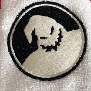 May include: White embroidered patch with a black outline, featuring a silhouette of a ghost with a stitched smile. The ghost is facing left and has a rounded head.