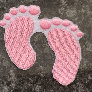 Può includere: Impronte di piedi di bambino ricamate in rosa su uno sfondo bianco.