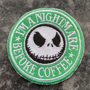 May include: A green and white embroidered patch featuring the text "The Nightmare Before Coffee" and a black and white image of Jack Skellington from the film "The Nightmare Before Christmas".