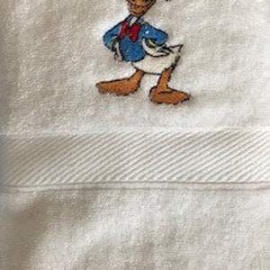Può includere: Asciugamano da bagno bianco con un'immagine ricamata di Paperino in un abito da marinaio blu.