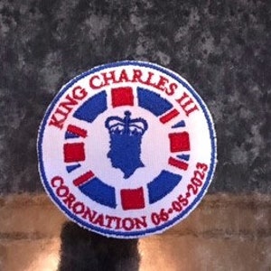 Może przedstawiać: Naszywka haftowana w kolorze białym, czerwonym i niebieskim z tekstem "King Charles III Coronation 06-05-2023". Naszywka przedstawia koronę i profil króla Karola III.