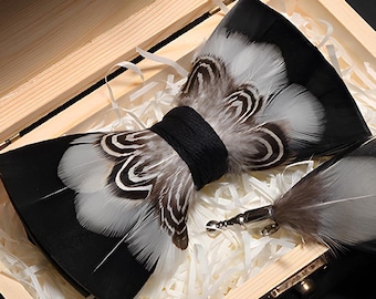 May include: A black and white feather bow tie with a matching feather lapel pin, both in a wooden box with white tissue paper.