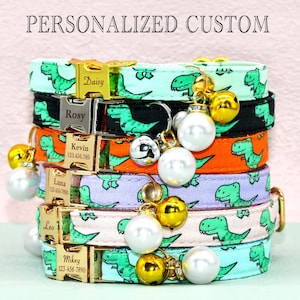 May include: A stack of six colorful cat collars with personalized name tags and bells. The collars feature a dinosaur print and are available in a variety of colors, including green, black, orange, purple, pink, and blue.