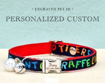 Può includere: Un collare per gatti rosso e nero con un'etichetta incisa in argento che dice "Daisy 123-456-7890". Il collare ha un motivo colorato con le parole "Notice" e "Raffle" su di esso. Il collare ha due campanelle d'argento attaccate ad esso.