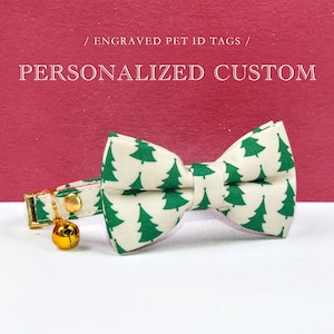 May include: A white cat collar with a green Christmas tree print bow tie and a gold bell. The collar is on a red and white background. / ENGRAVED PET ID TAGS / PERSONALIZED CUSTOM