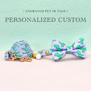 May include: A purple and green dog leash and bow tie set with a dinosaur print. The set includes a leash with a gold clasp and a bow tie with a green dinosaur pattern on a purple background. / ENGRAVED PET ID TAGS / PERSONALIZED CUSTOM